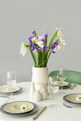 Dining table with stylish setting and vase with iris flowers served for International Women's Day celebration in room