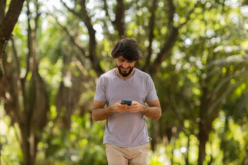 View of young man using a smartphone at day time with a green park in the background. High quality photo