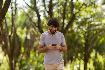 Naklejka na ściany i meble View of young man using a smartphone at day time with a green park in the background. High quality photo