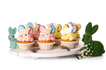 Board with tasty Easter cupcakes and bunnies on white background