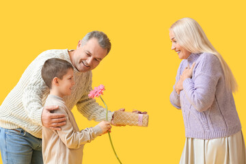 Senior man with little grandson greeting his wife on yellow background