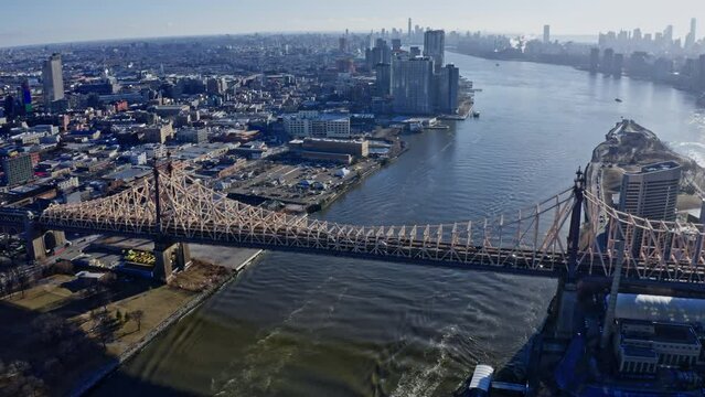 East River amidst buildings in city, drone flying backward from skyline