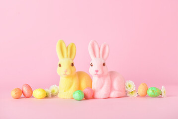 Cute Easter bunnies with eggs and flowers on pink background
