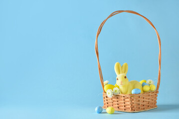 Fototapeta na wymiar Basket with cute Easter bunny and eggs on blue background