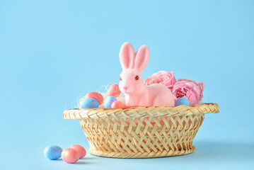 Basket with cute Easter bunny and eggs on blue background