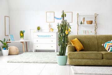 Interior of light living room with green sofa, cactus and Easter eggs