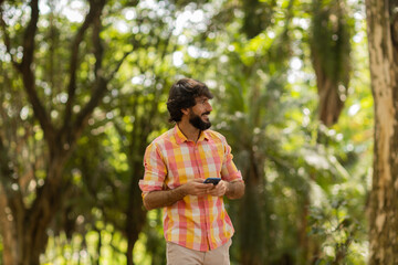 View of young man using a smartphone at day time with a green park in the background. High quality photo