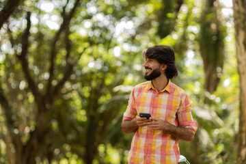 View of young man using a smartphone at day time with a green park in the background. High quality photo