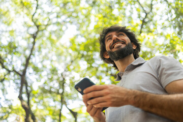 View of young man using a smartphone at day time with a green park in the background. High quality photo