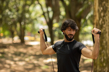 Strong man guy working out with elastic rubber bands at a park outdoors. Athlete male person during workout with additional sport equipment. High quality photo