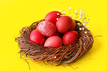 Nest with beautiful Easter eggs and flowers on yellow background