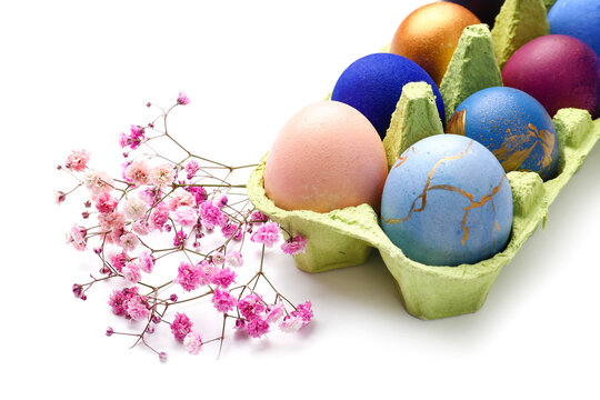 Holder with beautiful Easter eggs and gypsophila flowers on white background, closeup