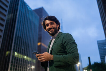 View of young man using a smartphone at night time with city view landscape in the background. High quality photo