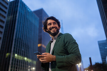 View of young man using a smartphone at night time with city view landscape in the background. High...