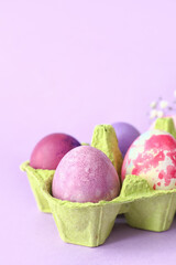 Holder with beautiful Easter eggs on lilac background, closeup