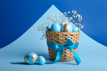 Basket with beautiful Easter eggs and flowers on blue background