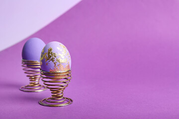 Holders with beautiful Easter eggs on purple background