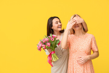 Beautiful woman with bouquet of flowers greeting her friend on color background. International...