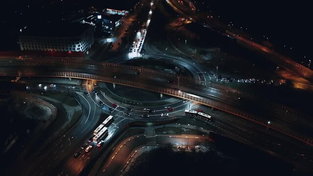 Aerial flyover car traffic roundabout interchange road at night, drone shot top down view expressway intersection in modern city in evening. Cars driving busy junction highway transportation