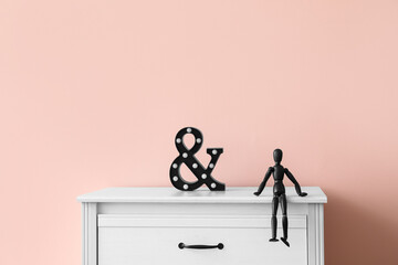 Wooden mannequin and ampersand symbol on chest of drawers near color wall