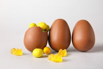 Chocolate Easter eggs with different candies on light background