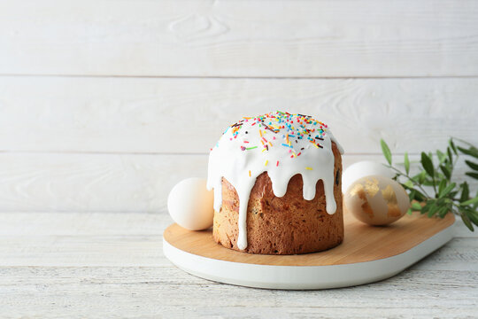 Board with delicious Easter cake and eggs on white wooden background