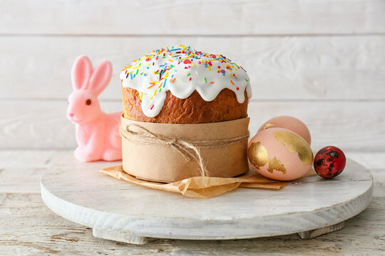Board with delicious Easter cake and eggs on white wooden background