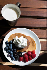 top view of pancakes with cream, blueberries and grapes with a glass of milk