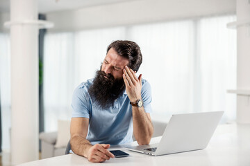 A bearded entrepreneur having a headache and migraine at home.
