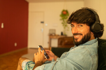 View of young man listening to music with headphones in his ears in the living room of his apartment. High quality photo.