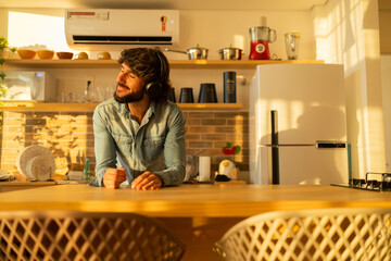 View of young man listening to music with headphones in his ears in the kitchen of his apartment. High quality photo.