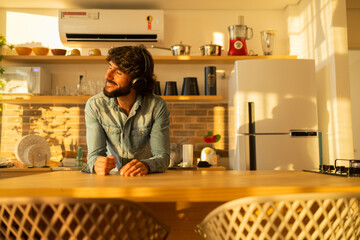 View of young man listening to music with headphones in his ears in the kitchen of his apartment. High quality photo.