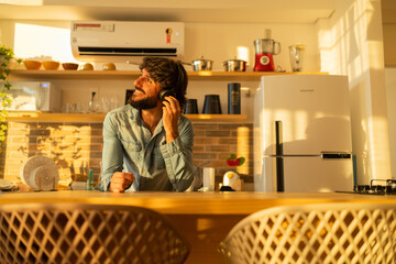 View of young man listening to music with headphones in his ears in the kitchen of his apartment. High quality photo.