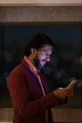 Side view of young man using a smartphone at night time with city view landscape in the background. High quality photo