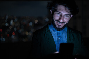 Front view of young man using a smartphone at night time with city view landscape in the background. High quality photo