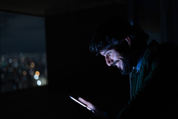Side view of young man using a smartphone at night time with city view landscape in the background. High quality photo