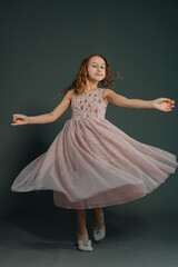 Photo in motion, a beautiful little girl in a fluffy soft pink dress is spinning on a plain gray...