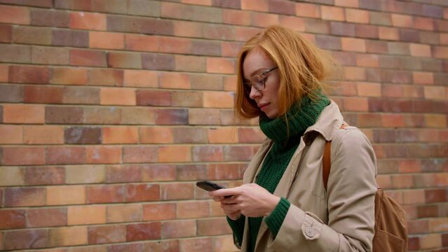 Mid adult woman using smartphone and walking against the brich wall in town.