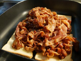 Metal tray of fried bacon strips on top of bread slices