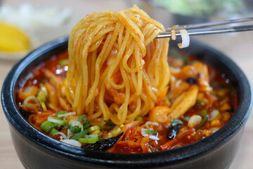 Pick up the jjamppong noodles in the earthen pot with chopsticks.