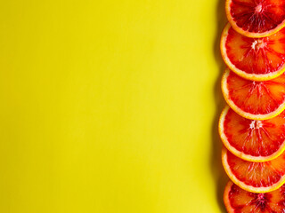 Border from red blood orange fruits slices isolated on yellow background. Flat lay, top view, copy space