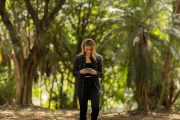 Young woman using a smartphone at day time with a green park in the background. High quality photo