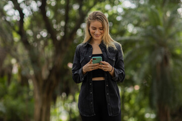 Young woman using a smartphone at day time with a green park in the background. High quality photo