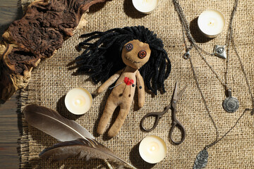 Voodoo doll with pins surrounded by ceremonial items on wooden table, flat lay