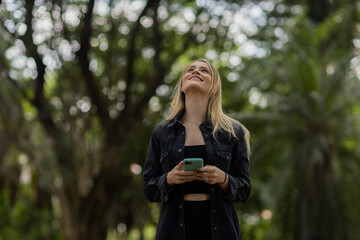 Young woman using a smartphone at day time with a green park in the background. High quality photo