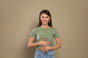 Healthy woman holding hands on belly against beige background - obrazy, fototapety, plakaty