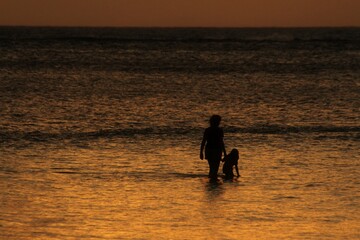 Fototapeta na wymiar Silhouette of a woman and a child wading in the beach at sunset