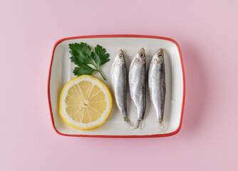 Salted sprat with lemon and parsley in a plate on a pink background. Flat lay.