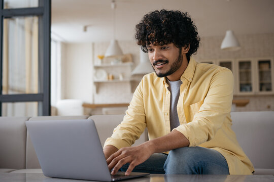 Handsome Indian business man using laptop computer, searching online, working from home. Smiling asian programmer typing on keyboard sitting at workplace. Successful business, freelance concept 