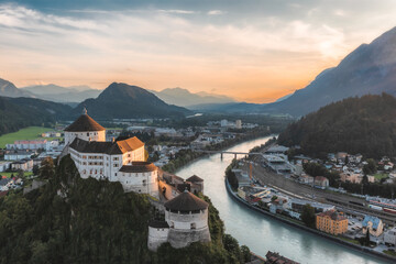 European Castle with river flowing by. City, mountain and sunset backdrop. Mountain town Kufstein with hilltop fortress